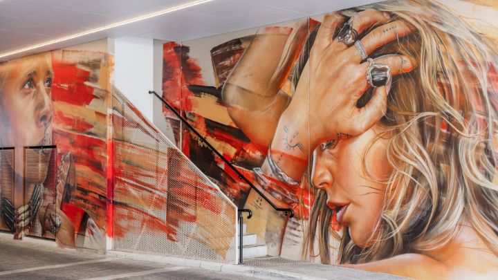 A stairwell with an abstract painted banister against a wall with a painted mural of faces